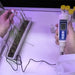 Person using a digital pH meter to test water next to a plant in a container.
