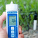 Digital pH meter held in a hand with a green outdoor background