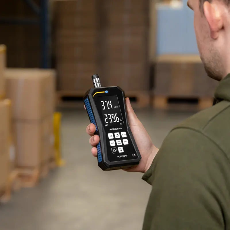 Person holding a digital thermometer in a warehouse setting