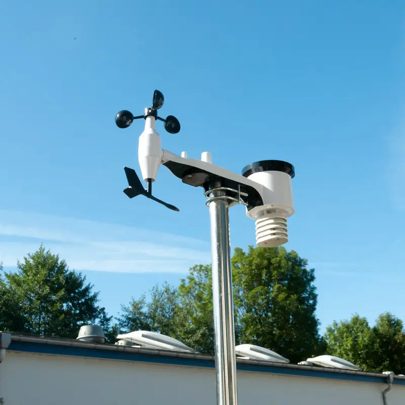 Weather station on a pole with a clear blue sky and trees in the background
