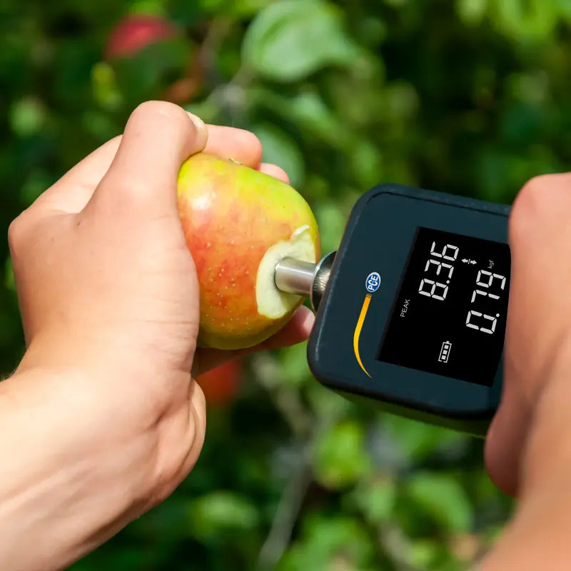 Hand using a Force Gage to measure an apple outdoors