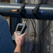 Person using a Ultrasonic Flow Meter to measure something on a pipe outdoors.