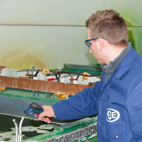 Person in a blue jacket with a GE logo using a tool in a workshop setting.