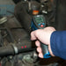 Hand holding a digital thermometer in front of a car engine