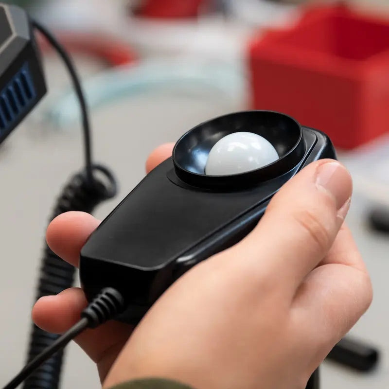 Hand holding a light meter with a white bulb inside, blurred background