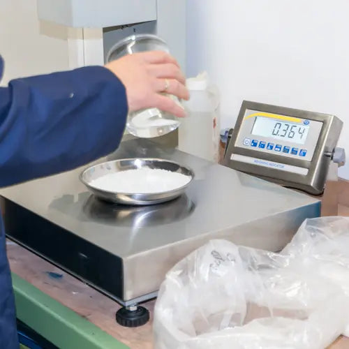 Person using a digital scale to measure powder, with a digital display showing weight.