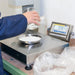 Person using a digital scale to measure powder, with a digital display showing weight.