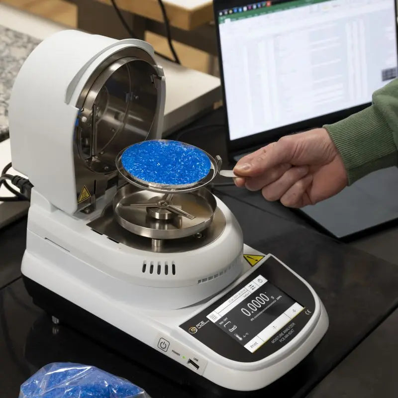 Person using a moisture analyzer with blue material on a desk.