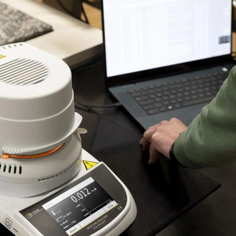 Person using a moisture analyzer with a laptop on a desk