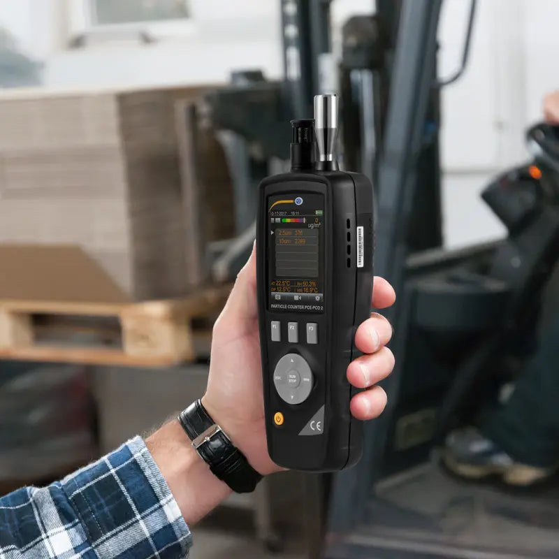 Hand holding a Particle counter in front of a forklift