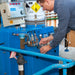 Person working on a blue industrial machine with various components and controls.