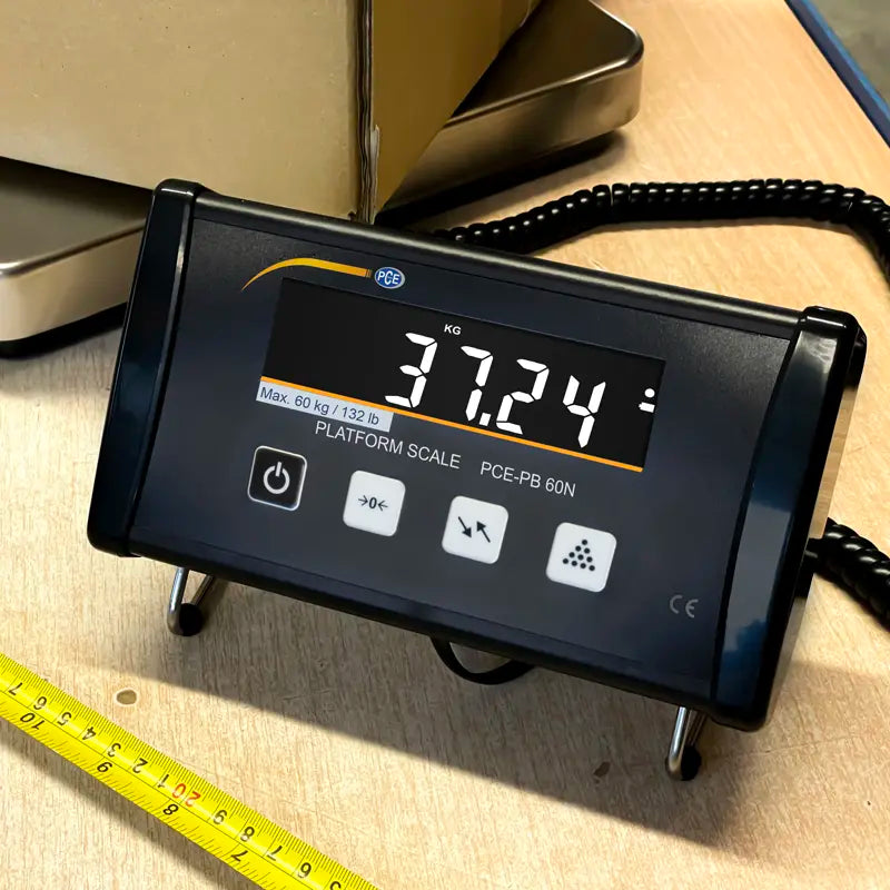 Digital platform scale displaying weight on a wooden surface with a measuring tape.