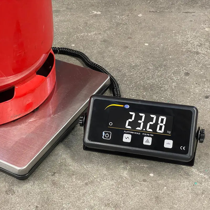 Digital scale displaying weight next to a red container on a concrete floor
