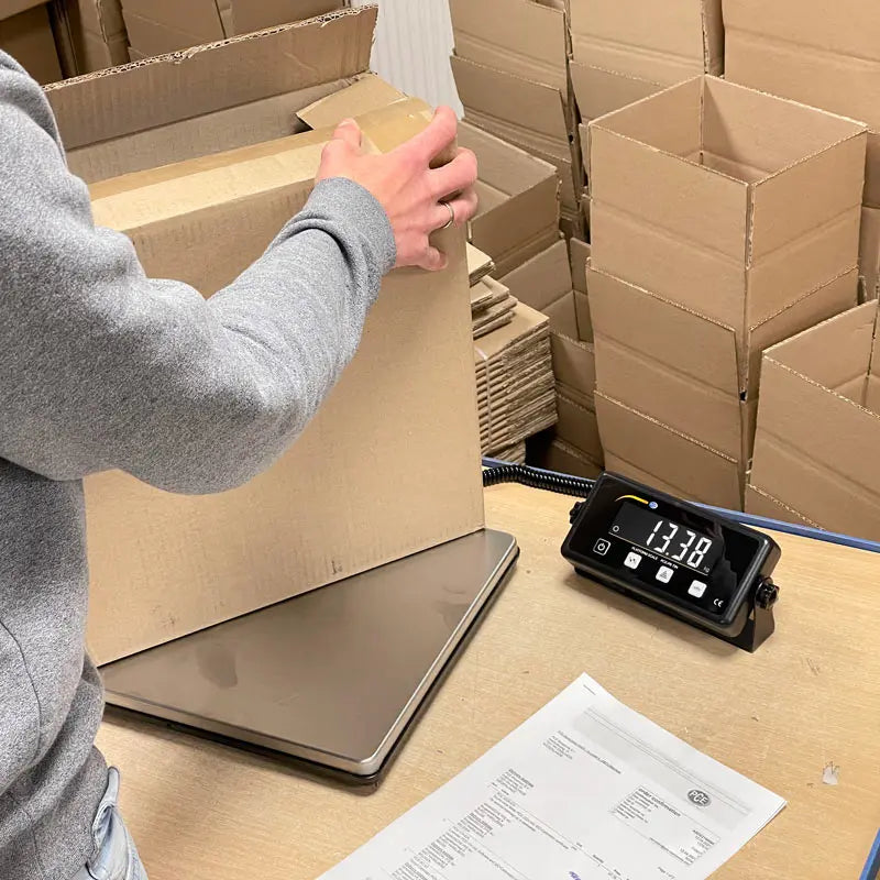 Person preparing a package with a digital scale on a table