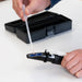 Person using a refractometer with a sample tube on a white surface