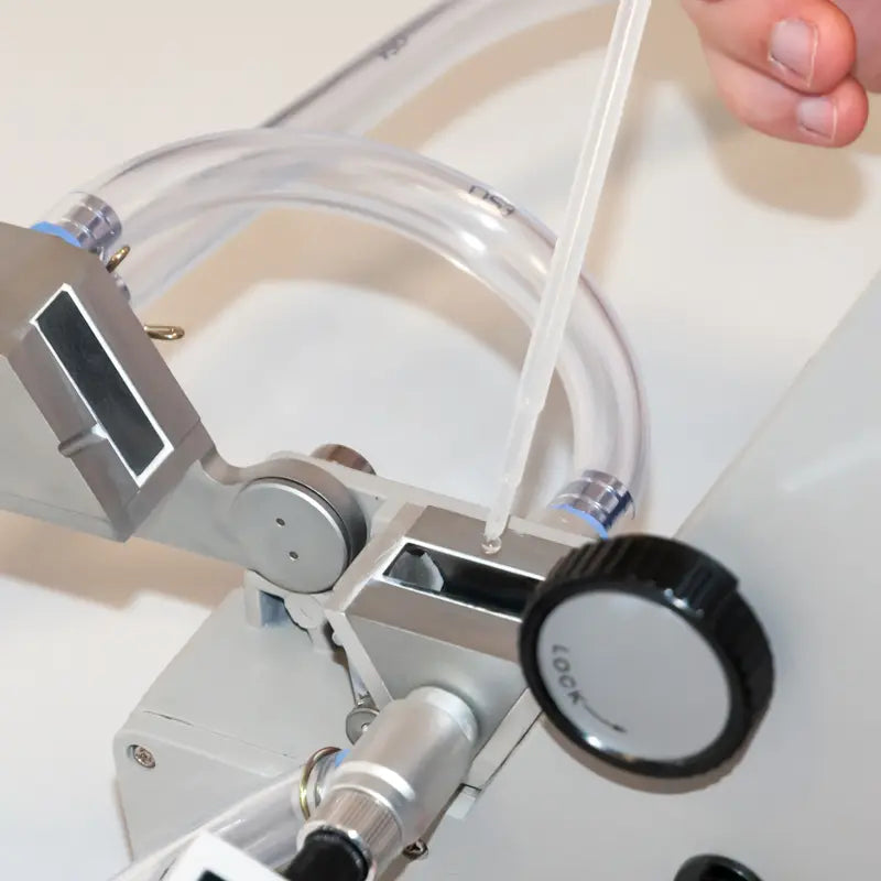 Close-up of a refractometer with a hand holding a tube, likely for administering medication.