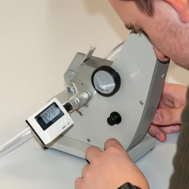 Person using a refractometer with a digital display on a light-colored surface.