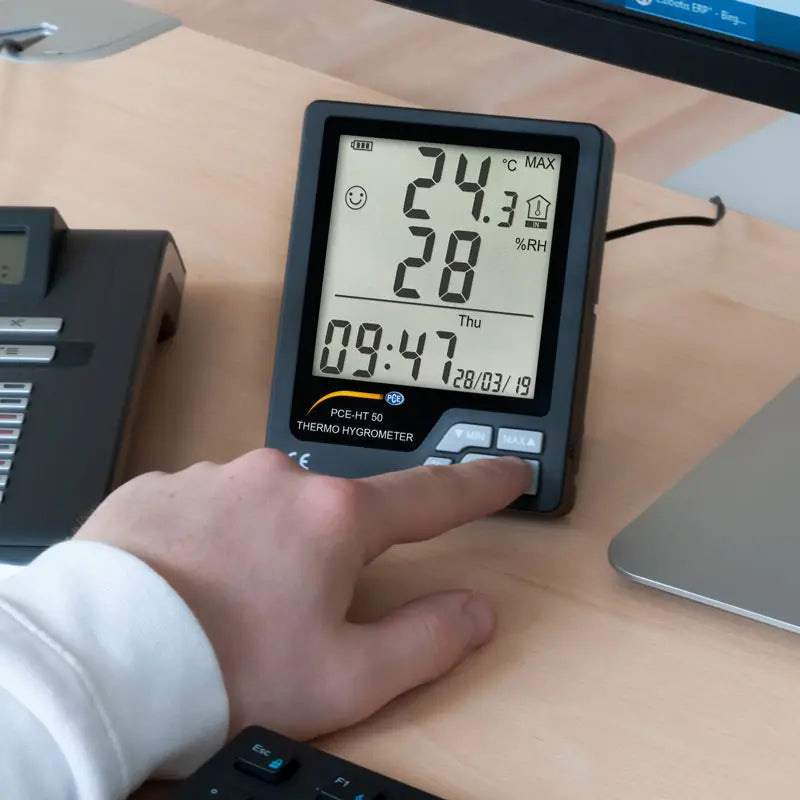 Digital thermometer on a desk with a hand interacting with it