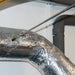Metal ductwork with reflective insulation against a white wall.