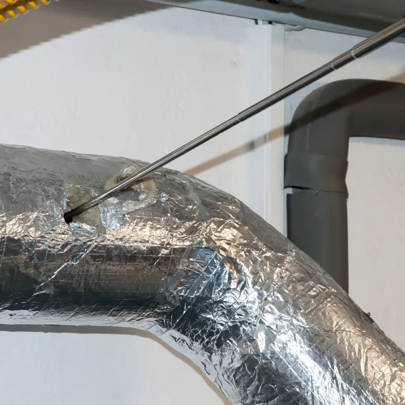 Metal ductwork with reflective insulation against a white wall.