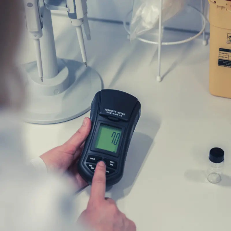 Person using a Turbidity Meter on a white surface with medical equipment in the background
