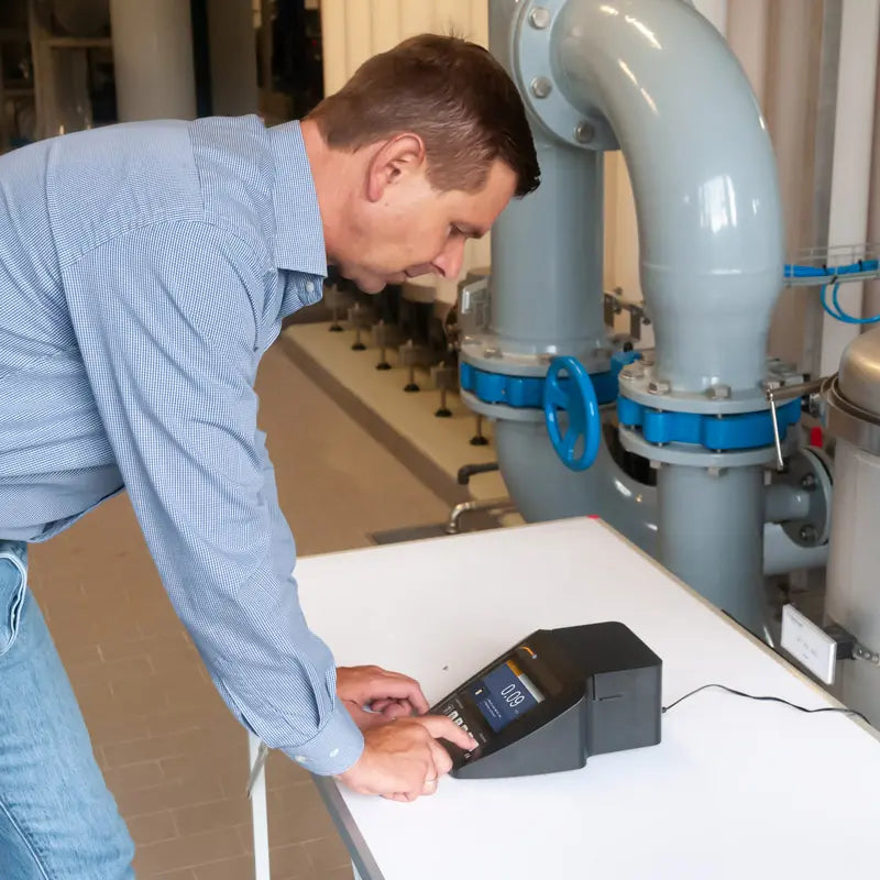Man using a Turbidity Meter near industrial pipes and equipment.