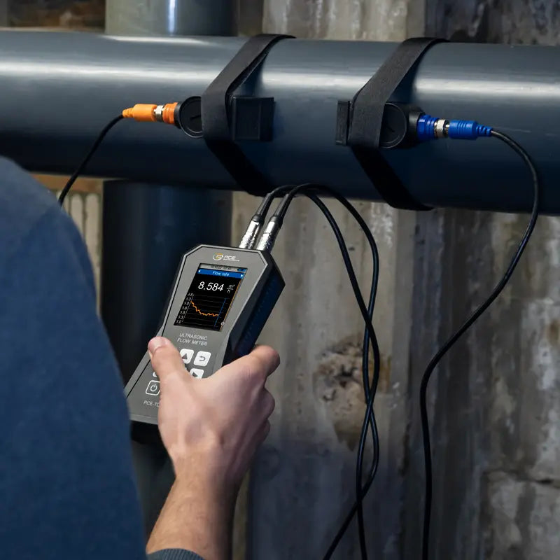 Person using a ultrasonic flow meter to measure something on a pipe outdoors.