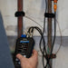 Hand holding an Ultrasonic Flow Meter measuring water flow and temperature next to pipes on a wall.