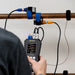 Person using an Ultrasonic Flow Meter on a pipe with visible measurement details.