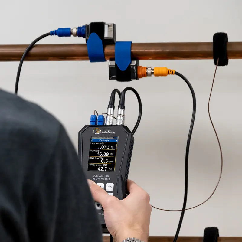 Person using an Ultrasonic Flow Meter on a pipe with visible measurement details.
