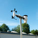 Weather station on a pole with a clear blue sky and trees in the background