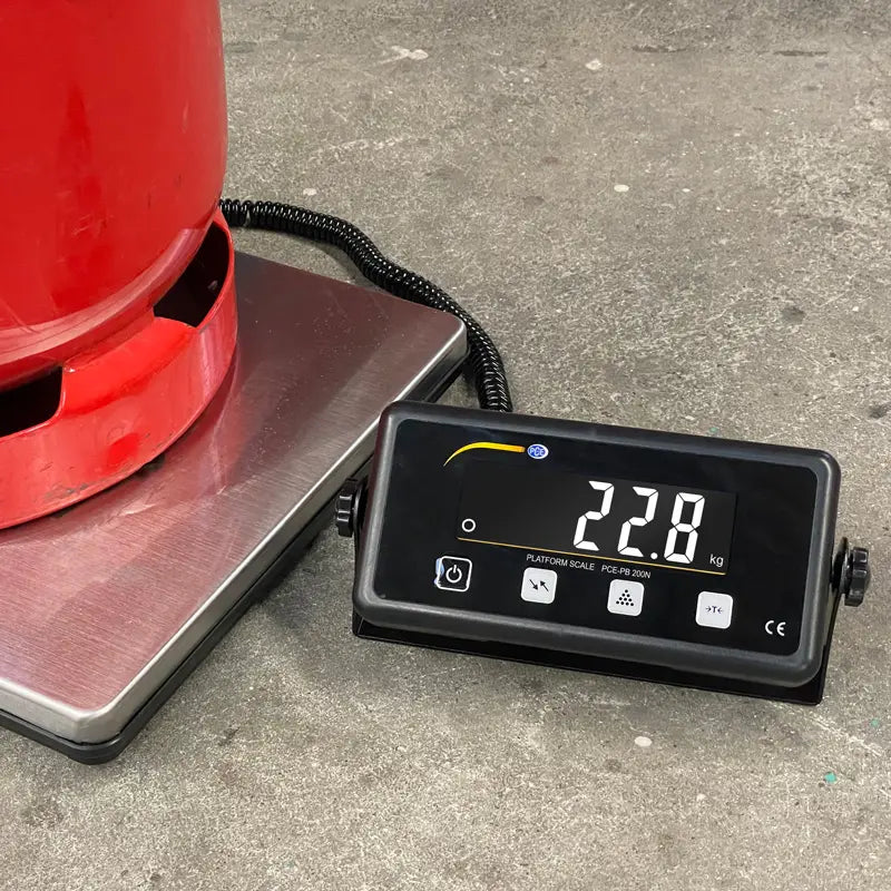 Digital scale with a red container on it, displaying weight on a concrete floor.