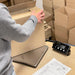 Person packaging a box on a digital scale with stacked boxes in the background